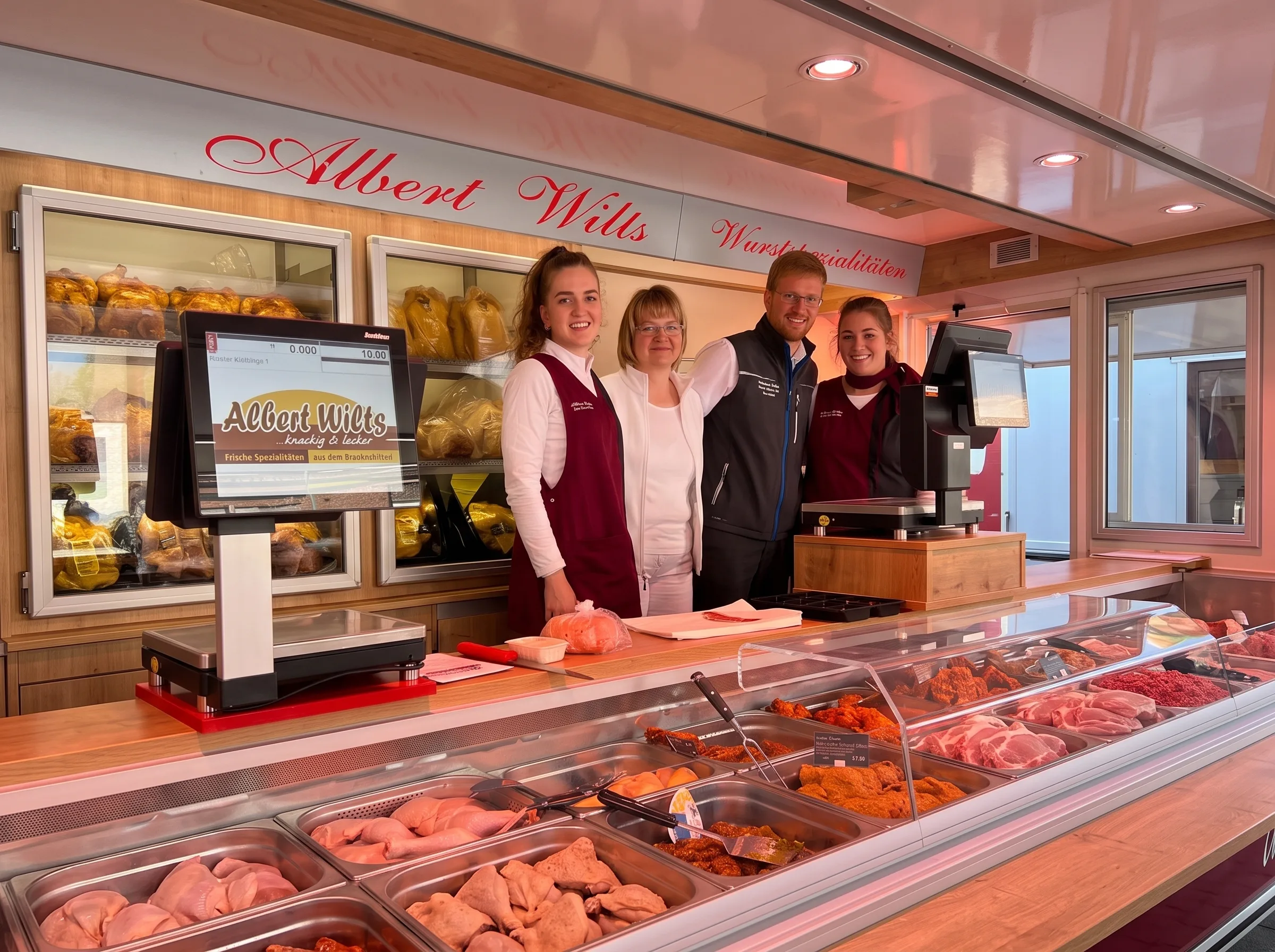 Familie Wilts mit Team am Verkaufswagen auf dem Wochenmarkt, davor die Frischetheke mit Geflügel und Wurst